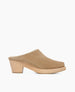 A tan suede mule with a wooden block heel, featuring a rounded toe and a plush, shearling-lined interior. 6