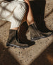 Dark olive green split suede ankle boots with a side zipper, squared toe, and a black treaded sole, worn with a cream-colored knit sweater. 6