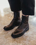 A person wearing black lace-up leather boots stands on a polished concrete floor. 11