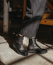 A person wearing black lace-up boots and dark pants stands on a concrete floor in a dimly lit room. 9