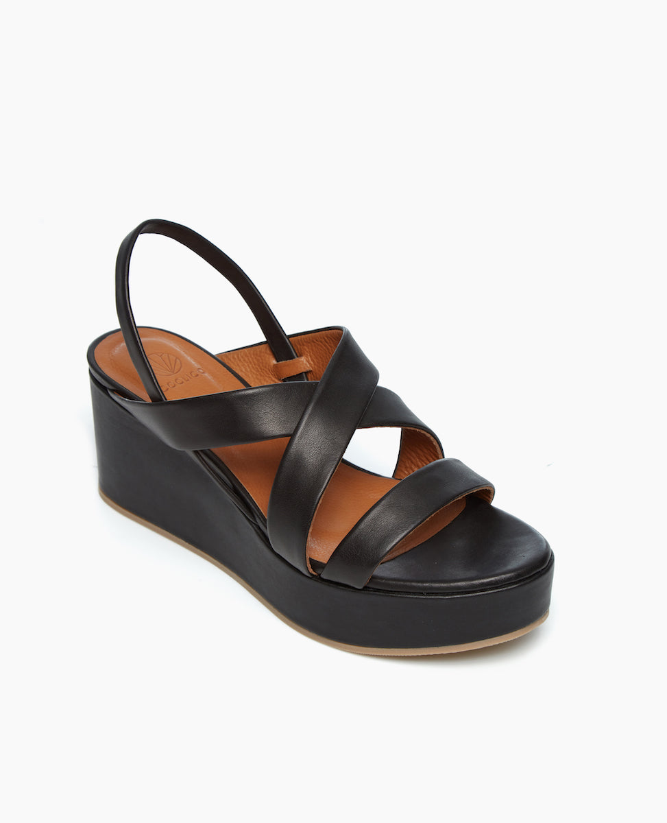 Angled view of leg lengthening, strappy Lylo Sandal in Black Leather featuring a lightweight, recycled cork wedge wrapped in leather. 