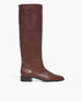 A tall, sleek, brown leather boot with a smooth texture, a round toe, a low block heel, and a minimalist design. 2