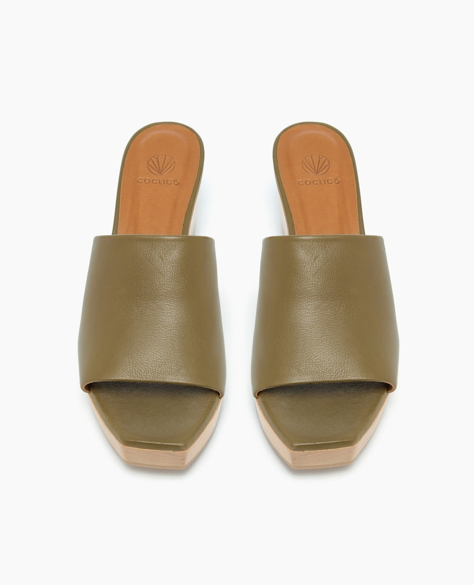 A pair of olive green, open-toe slide sandals with a smooth leather upper, tan leather insole, and a light wooden platform sole.