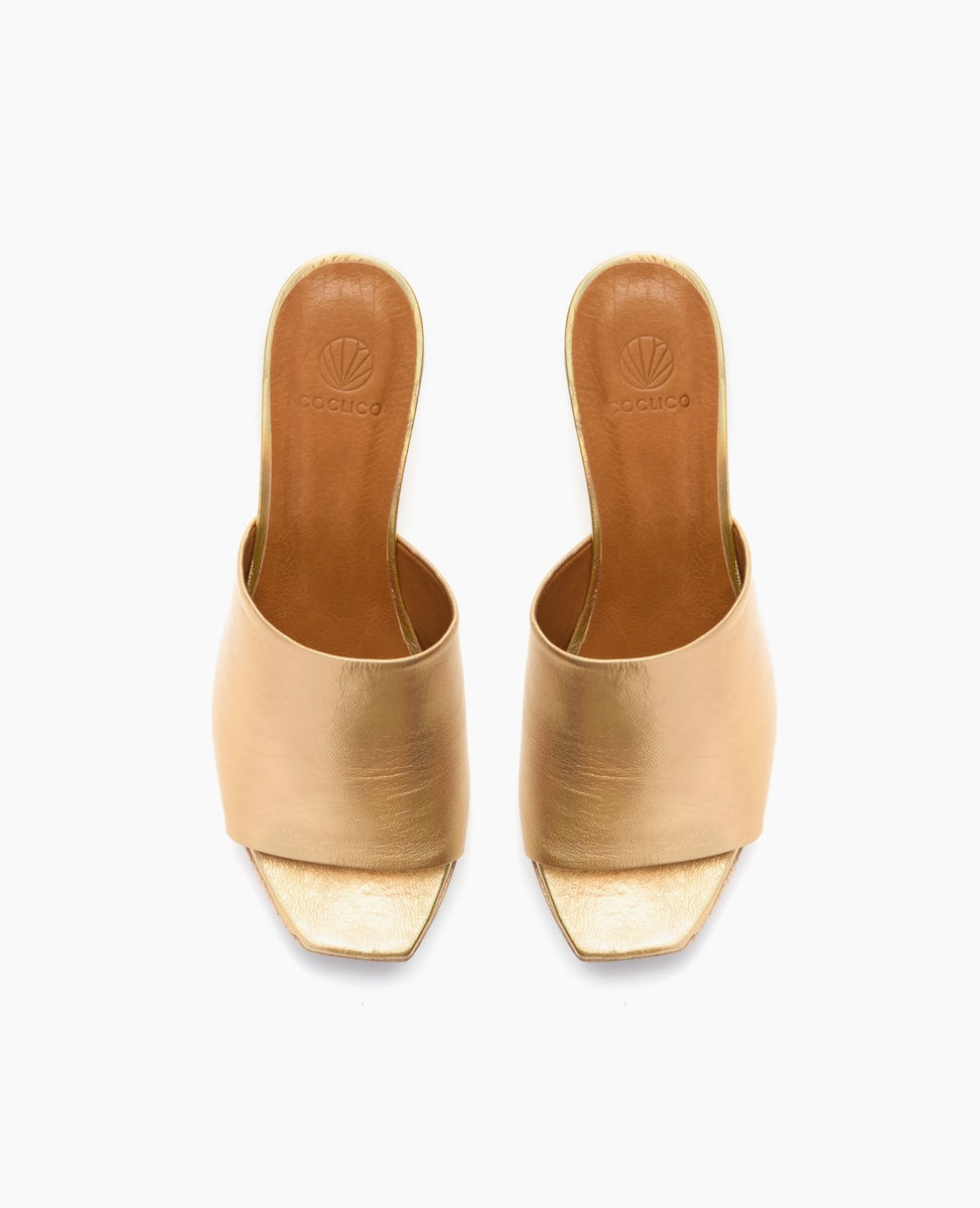 A pair of elegant, open-toed, gold metallic high-heeled mules with a square toe design and a smooth, shiny texture.