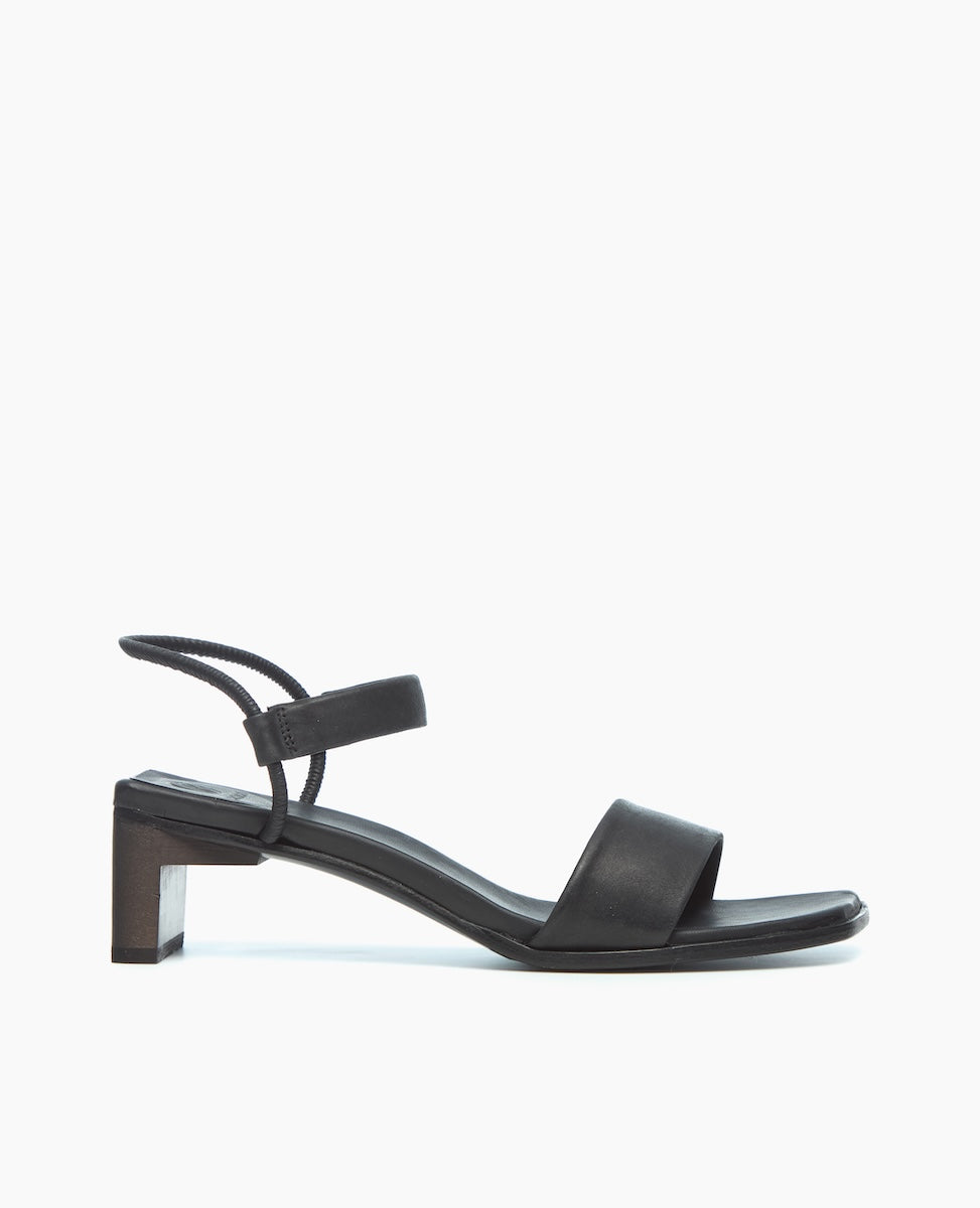 A sleek black sandal featuring a block heel, a wide front strap, and a thin ankle strap with a minimalist design.