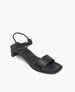 A sleek black sandal featuring a low block heel, a wide front strap, and a thin ankle strap with a minimalist design and smooth leather texture. 3