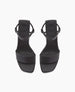 Black sandals with a minimalist design feature a smooth, matte finish, a single wide strap across the toes, an ankle strap with a buckle, and a flat sole. 4