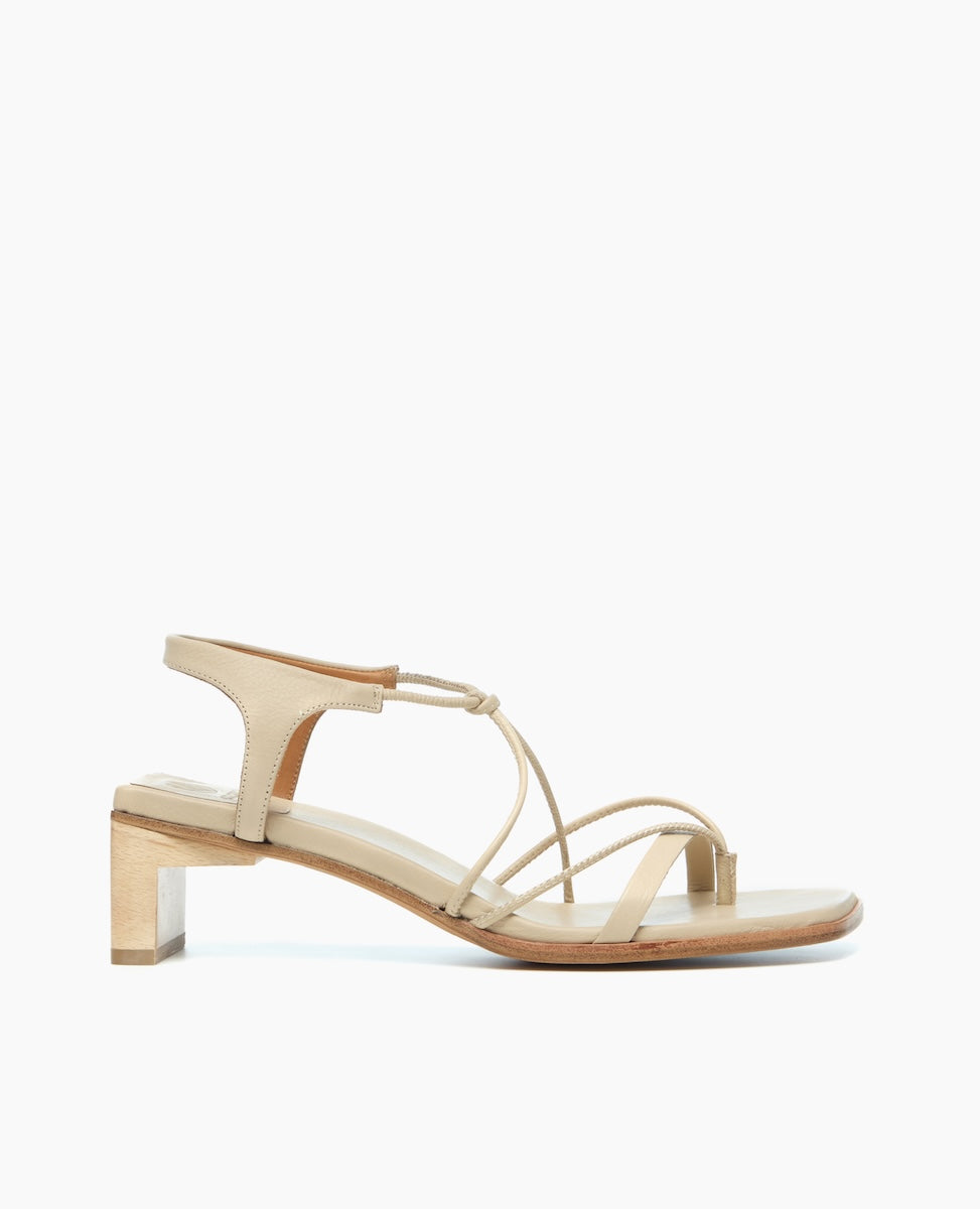 A beige sandal with a low block heel, featuring thin, delicate straps and a smooth leather finish.