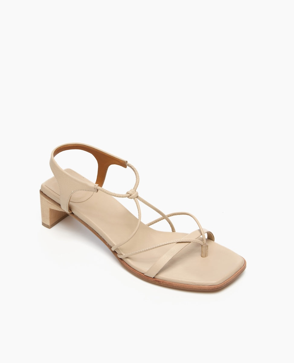 A beige sandal with a square toe, thin straps, a low block heel, and a smooth leather finish.