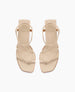 Beige sandals with a minimalist design feature thin straps, a square toe, and a flat sole, crafted from smooth leather with a subtle embossed logo on the insole. 4