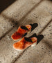 A pair of Autumn Leaf Shearling slippers with wooden soles are placed on a speckled concrete floor, illuminated by sunlight. 6