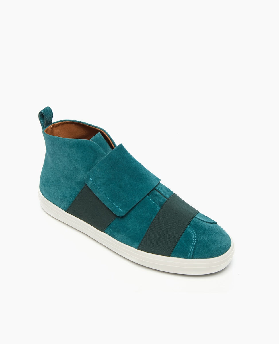 A teal suede high-top sneaker features a wide, dark green elastic strap across the top, a pull tab at the heel, and a white rubber sole.