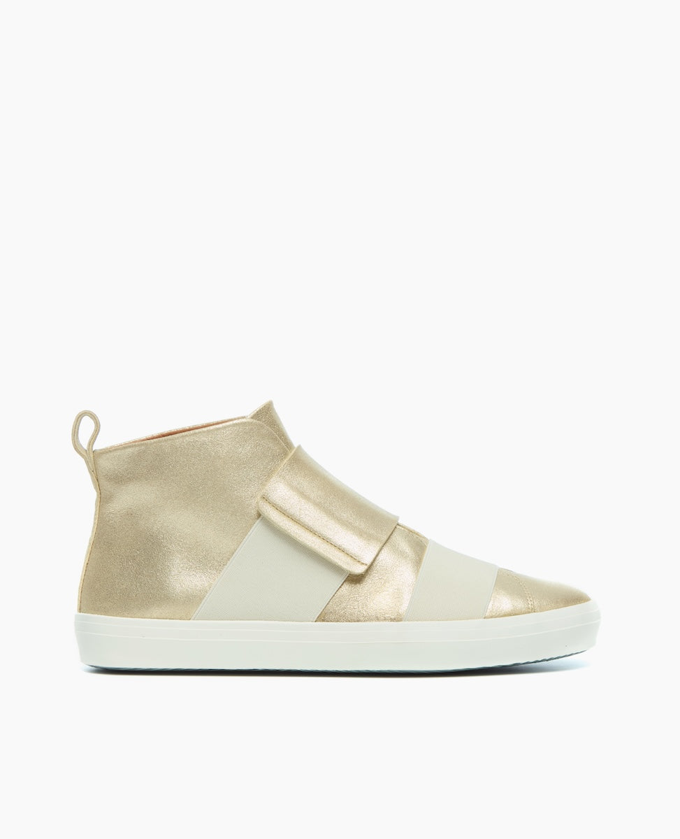 A stylish high-top sneaker featuring a metallic gold and cream color scheme, with a smooth texture, a wide strap across the front, a pull tab at the heel, and a white rubber sole.