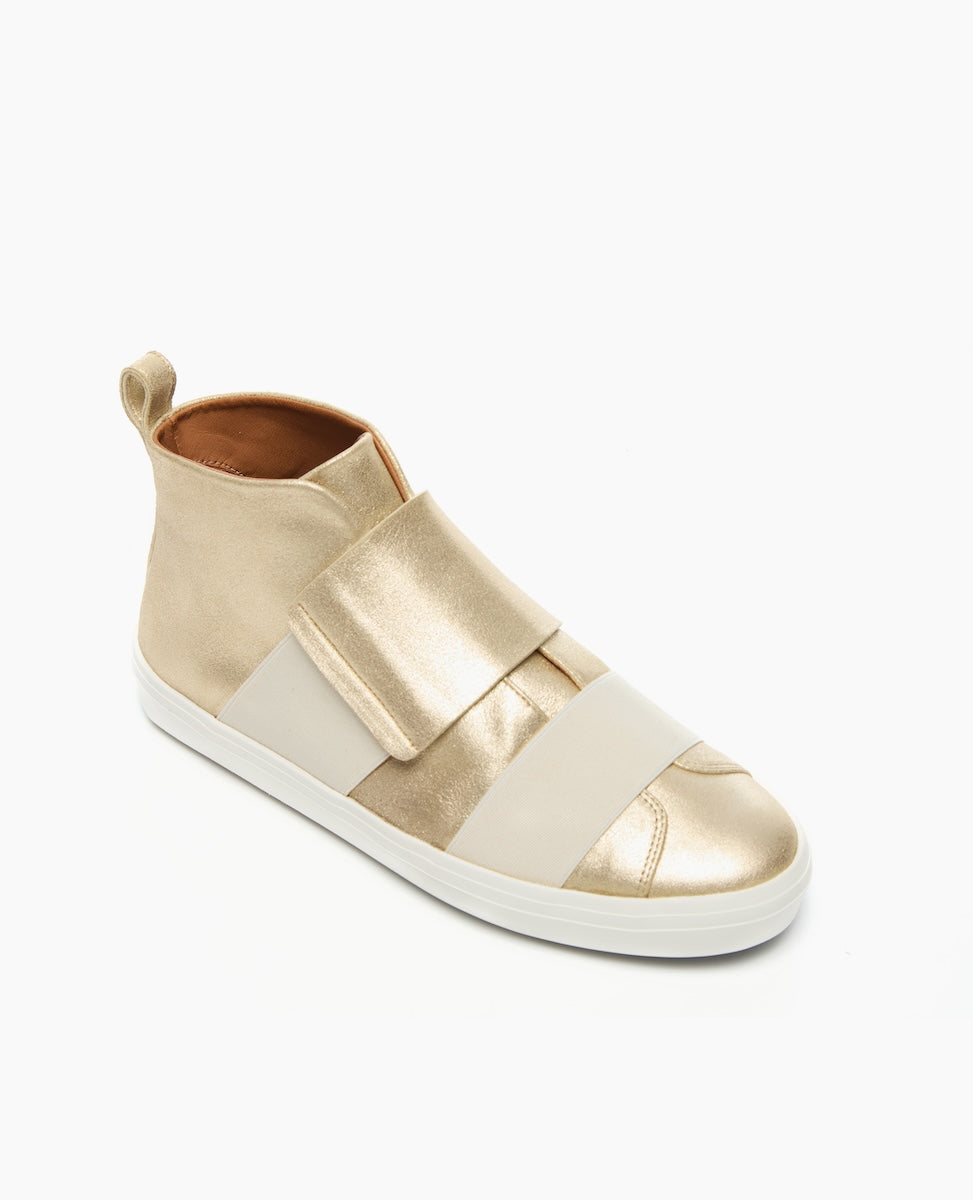 A sleek, gold high-top sneaker with a smooth, metallic finish, featuring wide beige elastic straps across the top, a white rubber sole, and a pull tab at the heel.