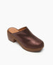 A brown, slip-on clog features a smooth, shiny leather upper with a rounded toe, a chunky wooden platform heel, and a simple, minimalist design. 6