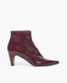 A sleek, burgundy ankle boot with a pointed toe, mid-height cone heel, crinkled patent leather texture, and a side zipper closure. 6