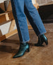 A person wearing blue jeans and teal ankle boots stands on a polished concrete floor near a wooden bench. 9