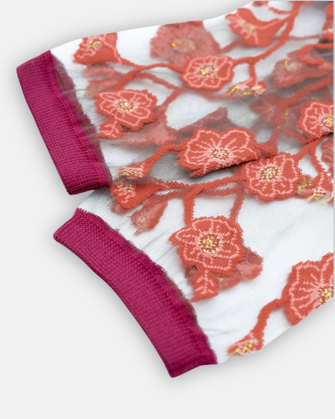 Pair of sheer Blomst Corail socks with coral flower embroidery and magenta cuffs, laid flat on a light gray background
