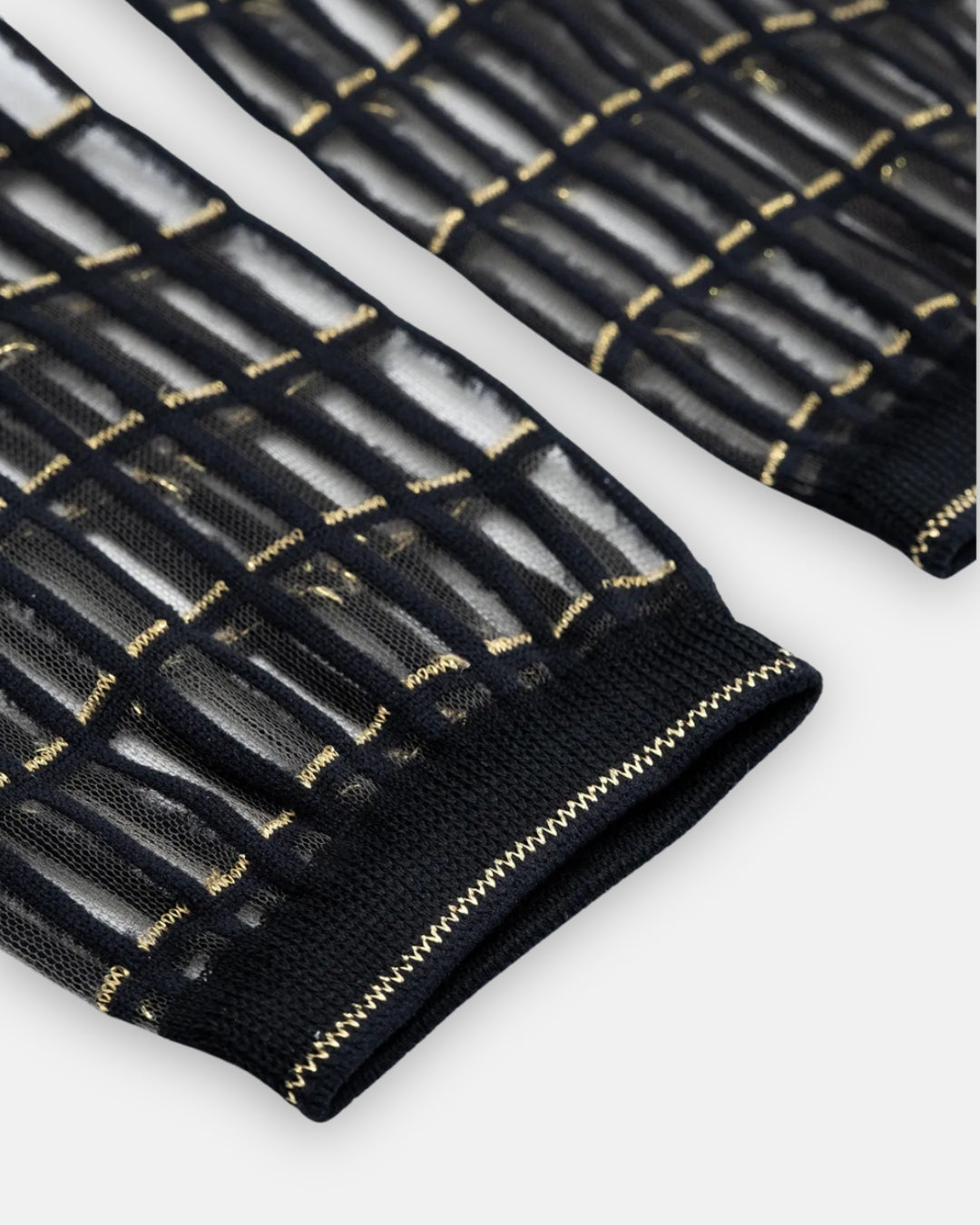 Pair of sheer black Blox Gold socks with a raised grid pattern and gold metallic stitching, laid flat on a light gray background
