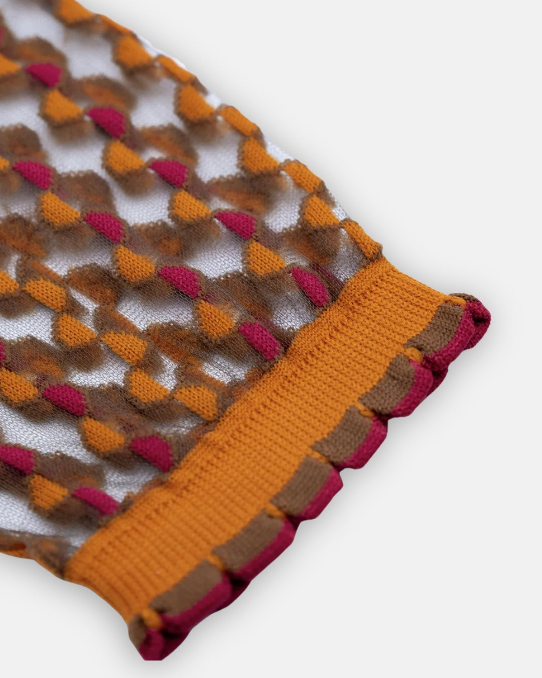 Sheer Cirkelbroen Ambre sock with an amber and raspberry woven pattern and amber cuff, laid flat on a light gray background
