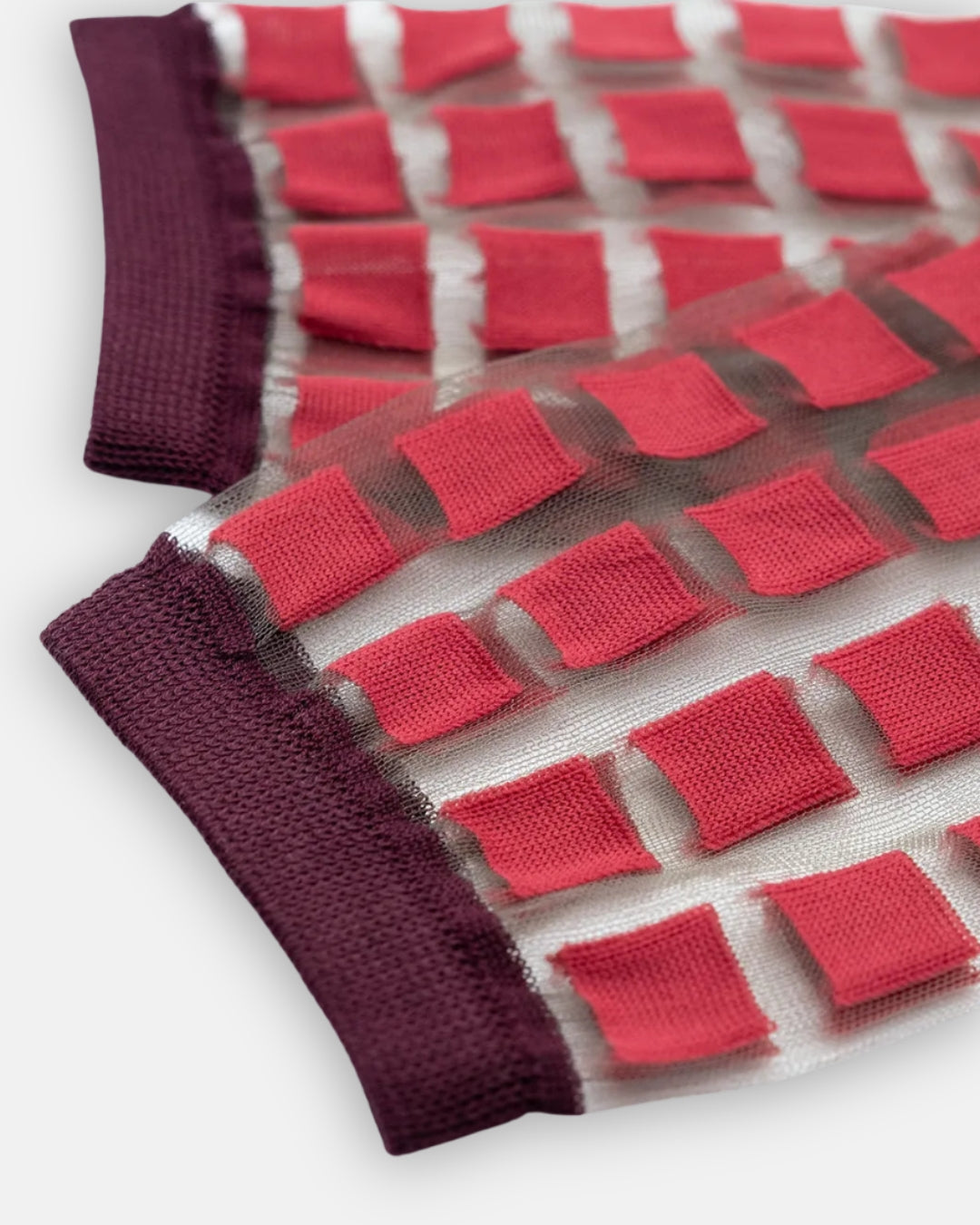 Pair of sheer Ginza Cerise socks with raised red squares in a grid and burgundy cuffs, laid flat on a light gray background