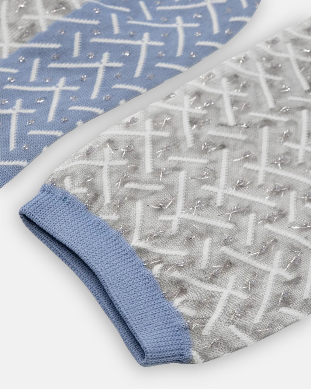 Pair of sheer Kaktus Polaire socks with a white crisscross pattern, silver flecks and light blue cuffs, laid flat on a light gray background