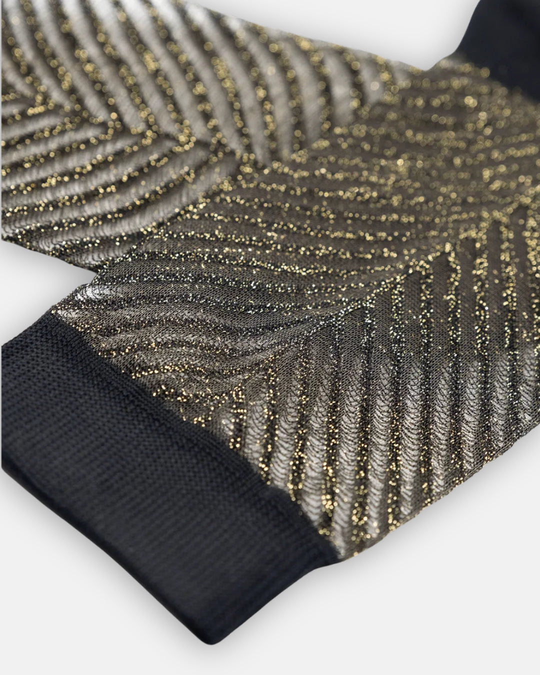 Sheer Sapin Doré sock with a gold metallic chevron pattern and black cuff, laid flat on a light gray background