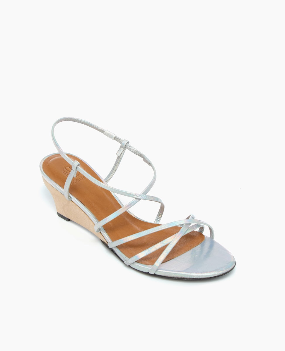 A sleek, silver strappy sandal with a low wedge heel, featuring a minimalist design with thin, metallic straps and a smooth, tan insole.