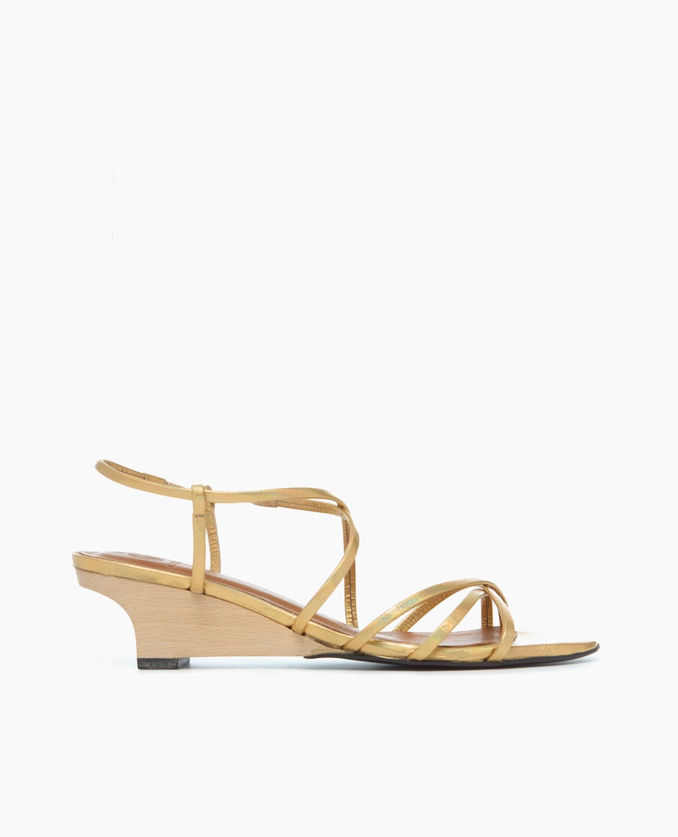 A sleek, tan sandal with thin, crisscrossing leather straps, a low wooden wedge heel, and a minimalist design.