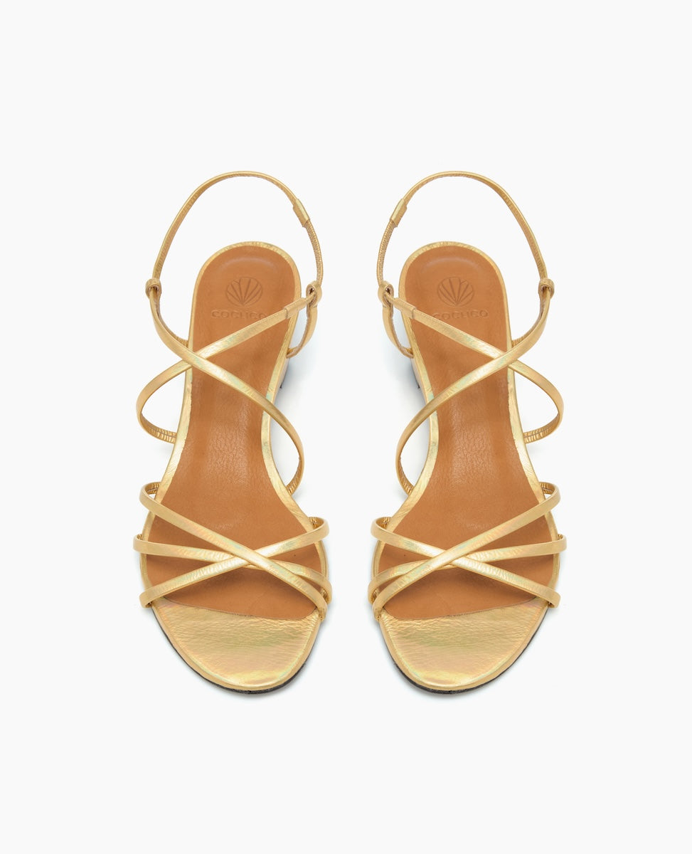 Elegant gold strappy sandals with a smooth, shiny finish, featuring a crisscross design over the foot, a slim ankle strap with a buckle, and a tan insole with a subtle embossed logo.