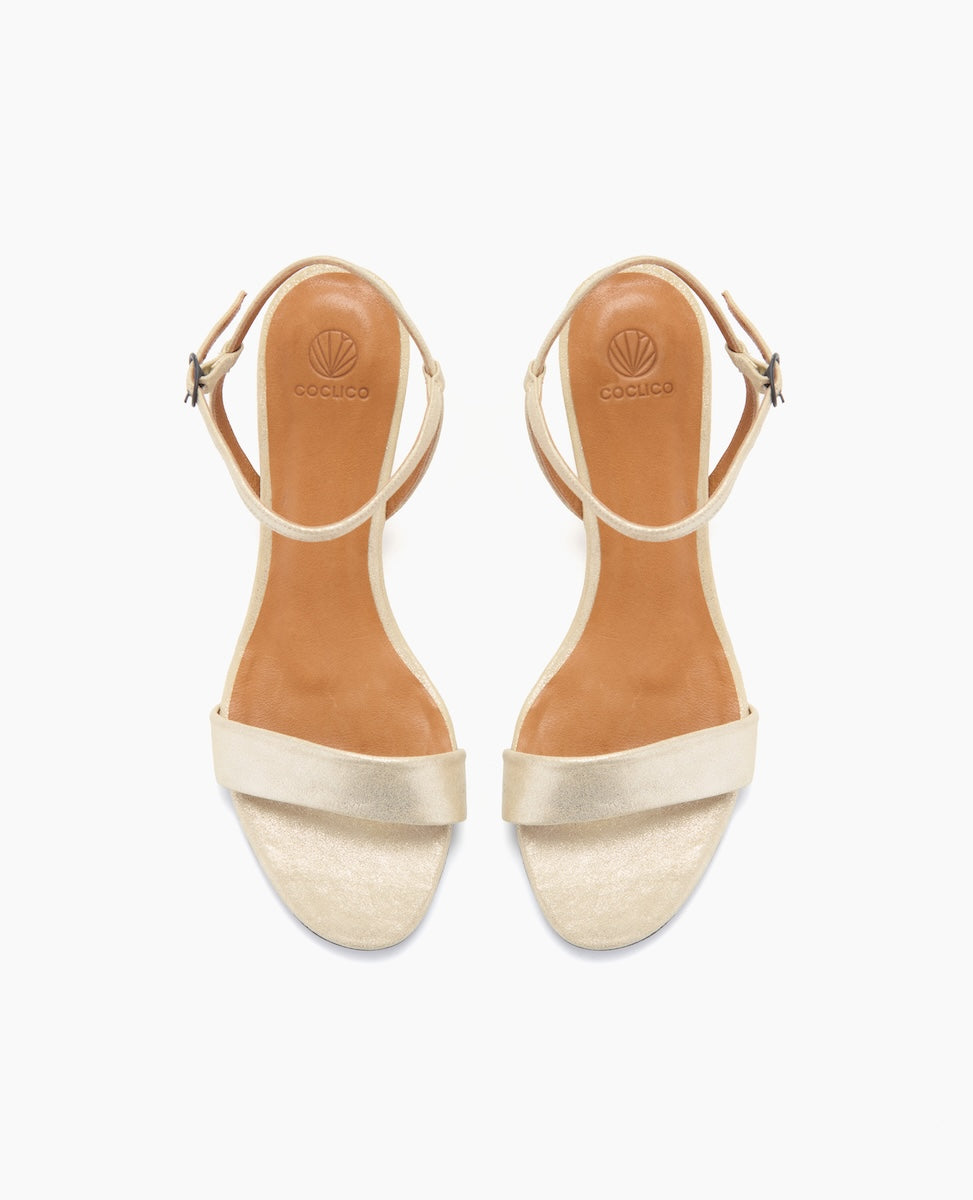 Beige open-toe sandals with a smooth leather finish, featuring a single wide strap across the toes, an adjustable ankle strap with a metallic buckle, and a tan insole embossed with a logo.