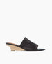 A sleek, black leather slide sandal with a smooth texture, featuring a minimalist design and a light wooden wedge heel. 2