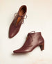 Coclico Booties in Merlot Leather with the left shoe laying on its side.  5