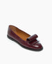 A single burgundy leather flat shoe with a decorative bow on the front and a black sole is displayed against a plain white background. 5