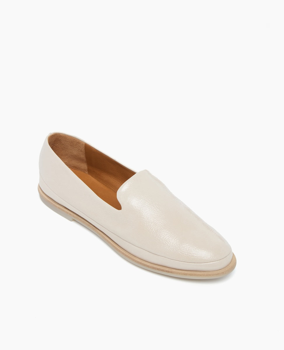 A sleek, cream-colored leather loafer with a smooth texture, featuring a rounded toe, low heel, and tan interior lining.