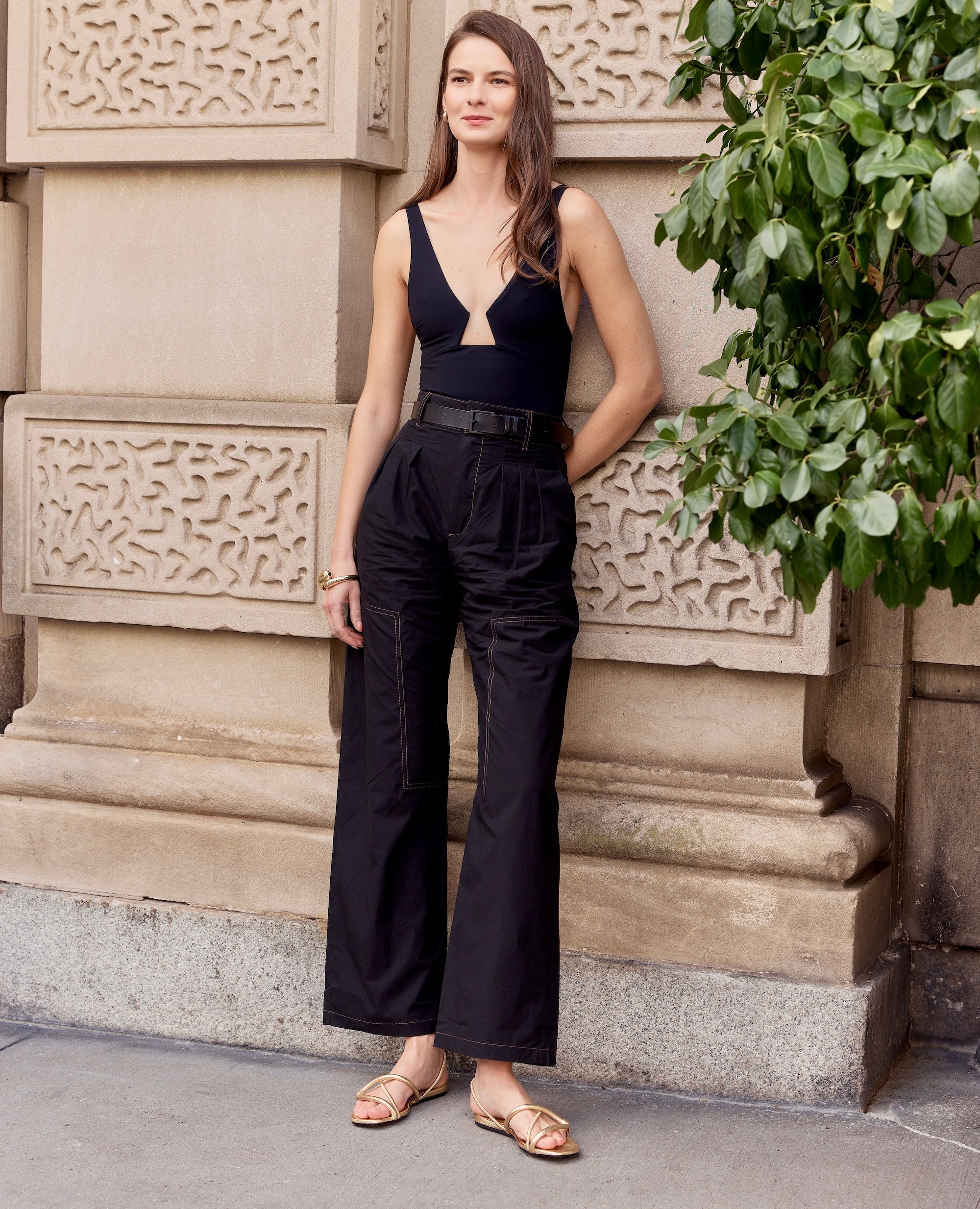 Woman in a black outfit  and gold sandals standing against an architectural background
