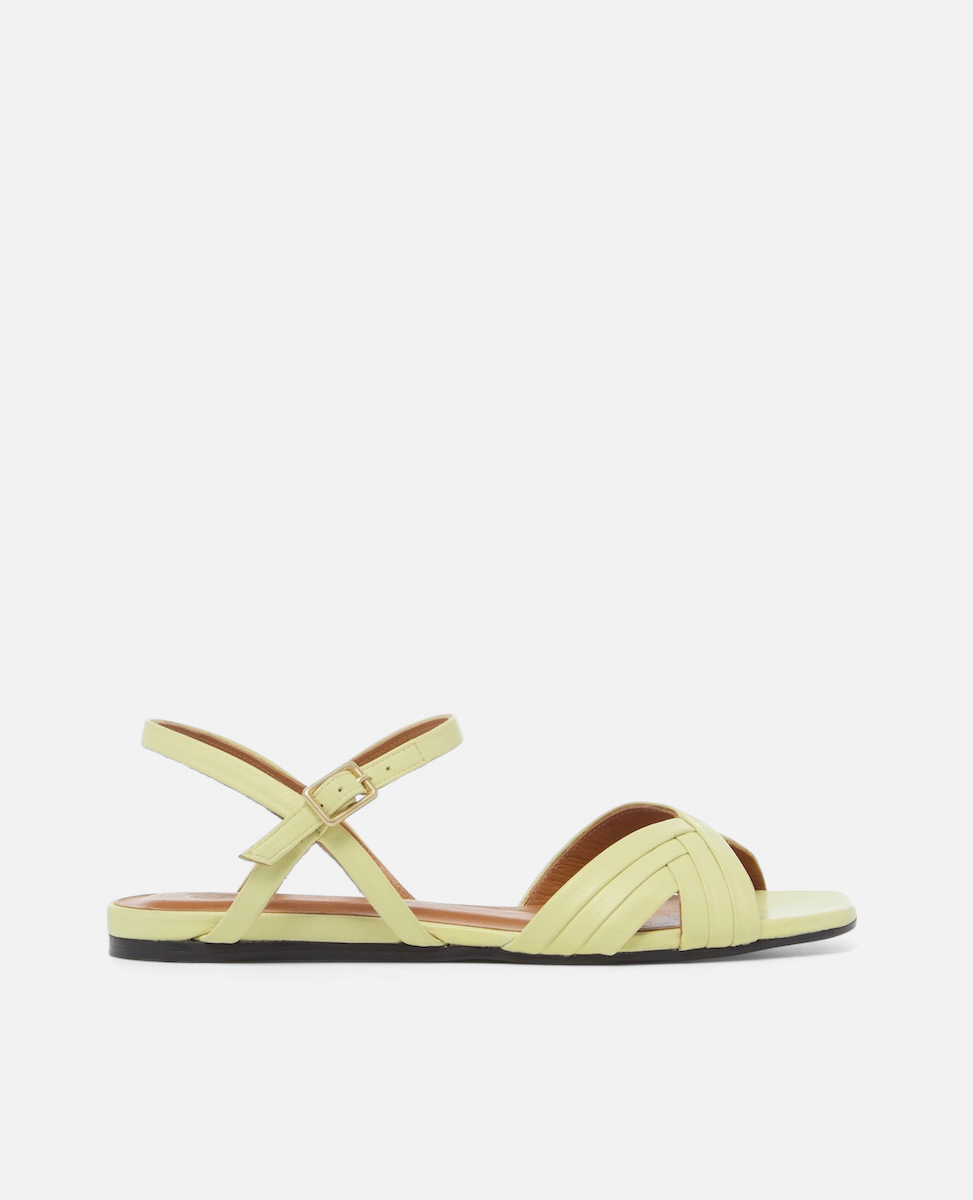 Side view of a pale yellow leather flat sandal with slim crisscross toe straps, buckle quarter strap, and square toe, on a white background.