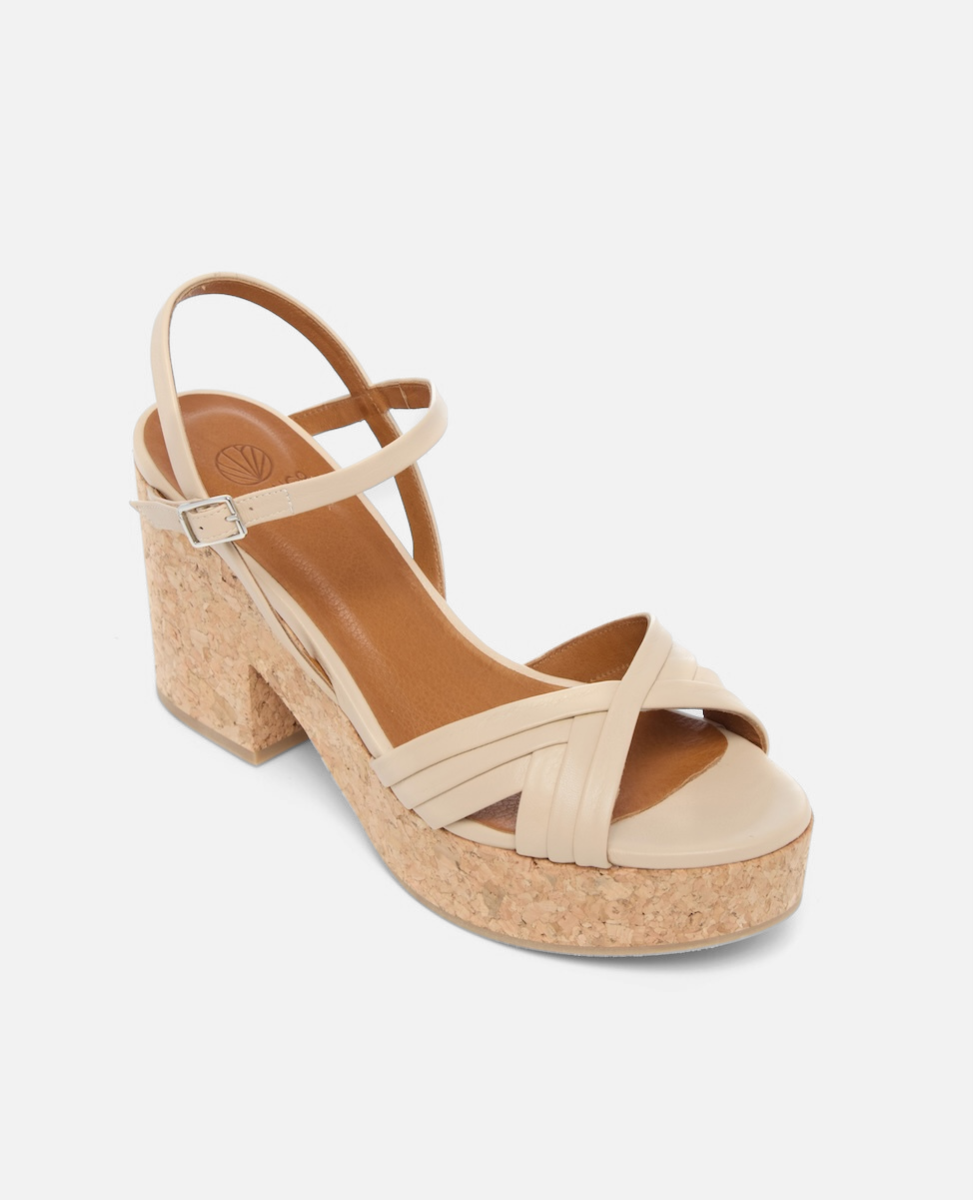 A beige sandal with a cork platform heel features crisscrossing straps at the toe, a single ankle strap, and a smooth, matte finish.