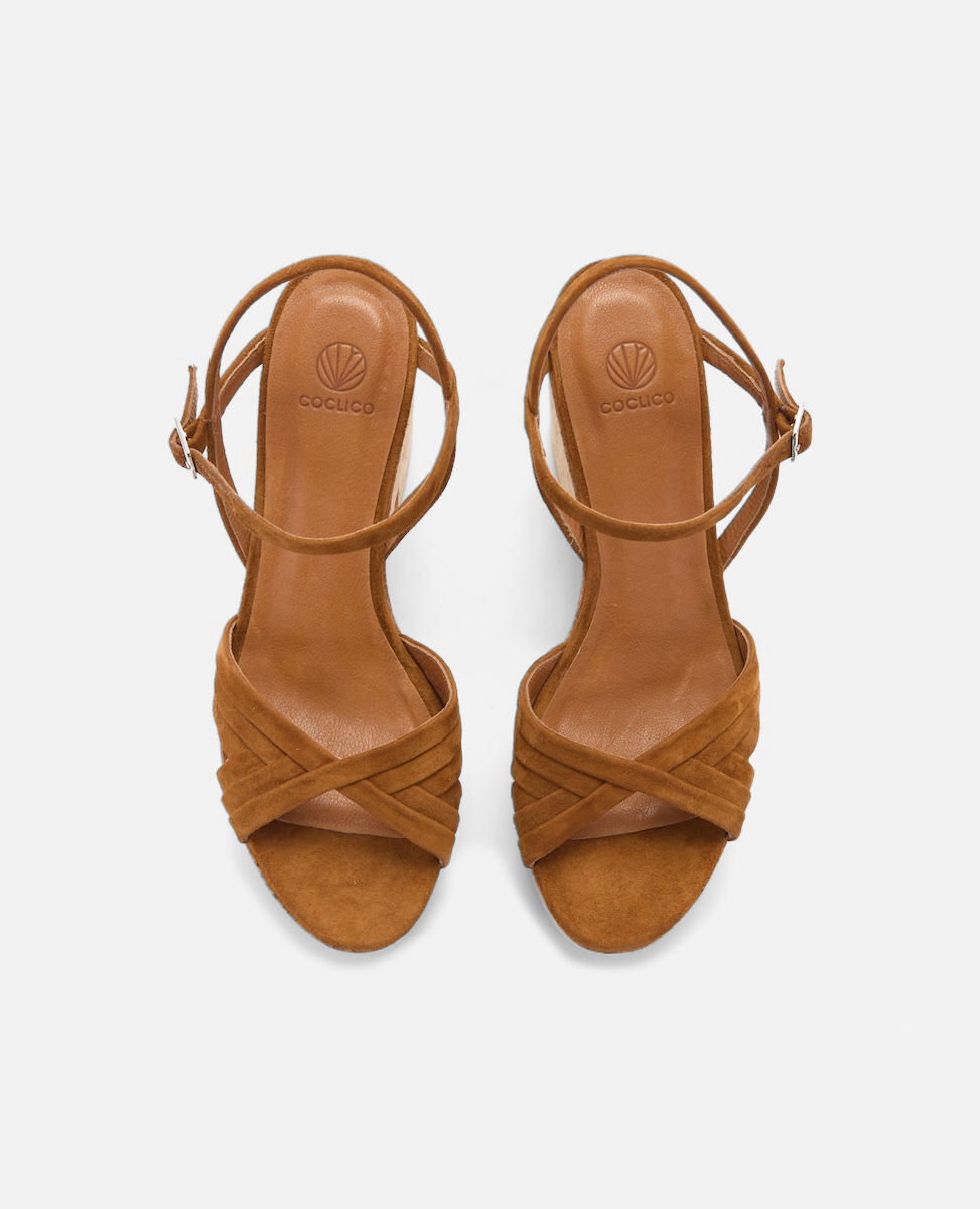 Brown suede sandals with a crisscross strap design, open toe, ankle strap with buckle, and a smooth leather insole featuring a logo imprint.