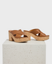 These sandals feature a brown leather upper with wide crisscross straps, a chunky cork platform heel, and an open-toe design, combining a smooth texture with a natural, earthy aesthetic. 1