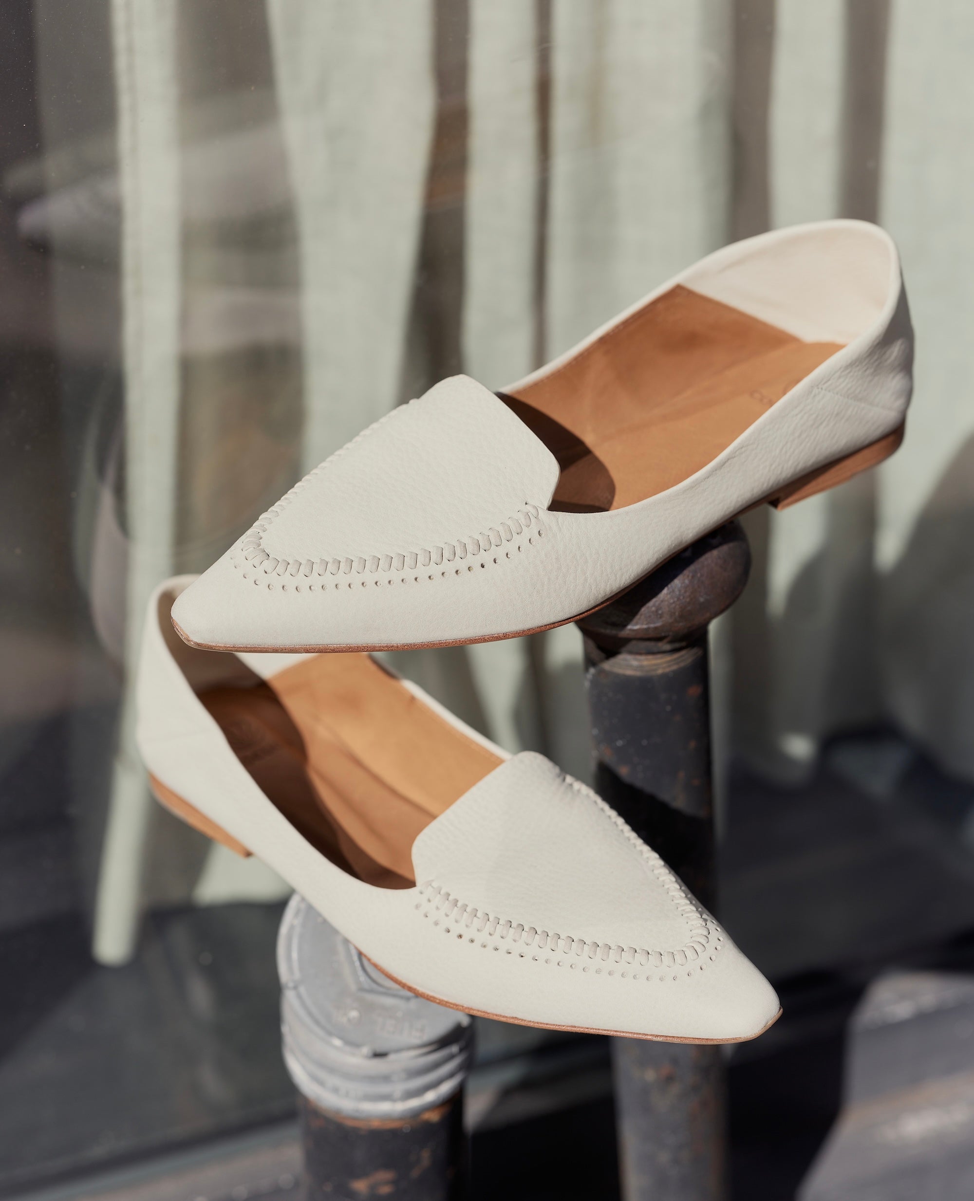 White loafers with brown soles on a metal stand against a window background