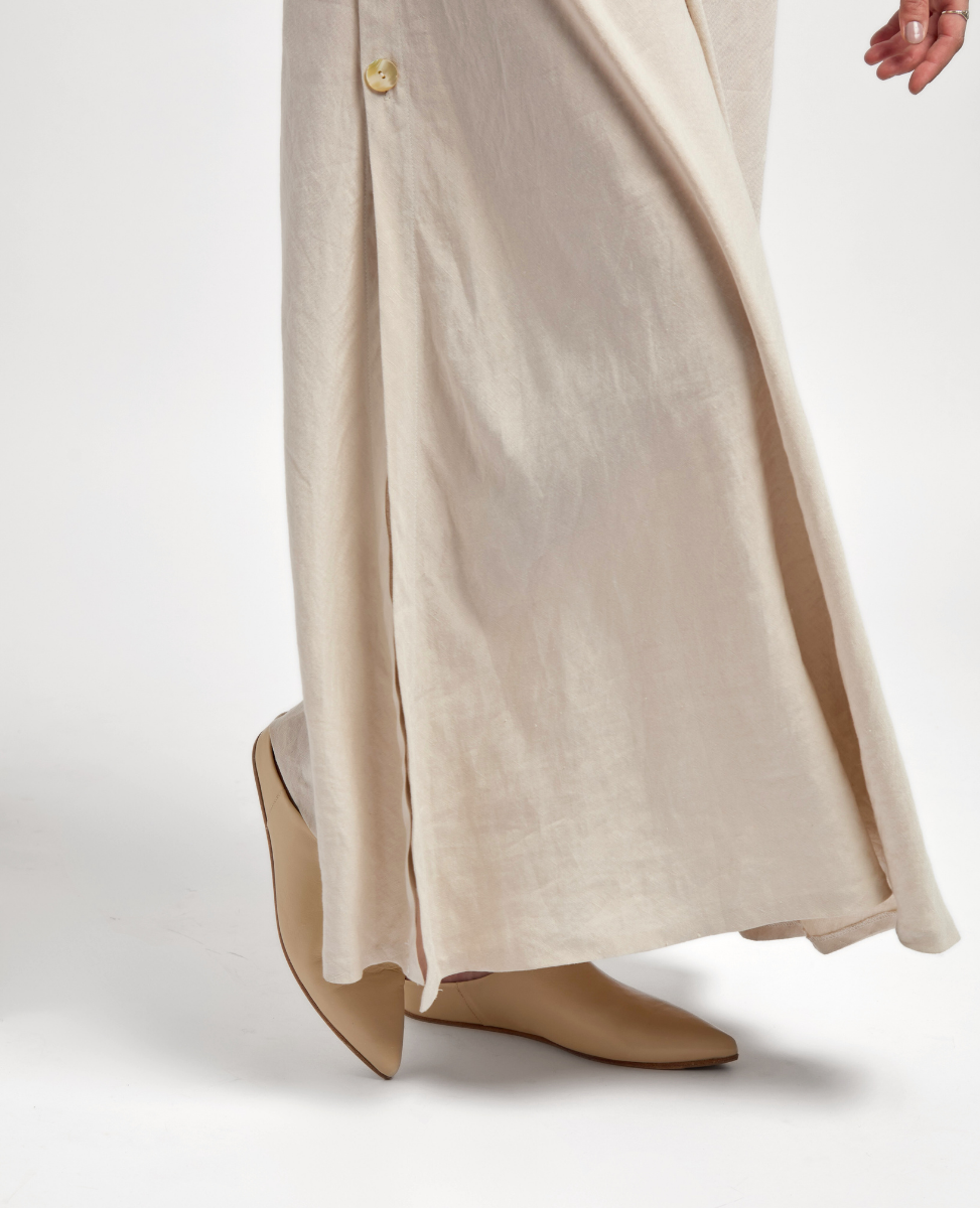 A long, flowing beige skirt with a subtle sheen, featuring a side button detail, is paired with sleek, pointed-toe tan boots.