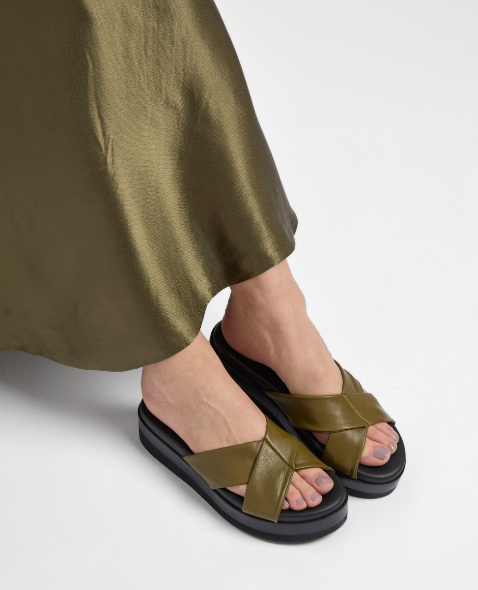 Olive green leather sandals feature wide crisscross straps, a cushioned black platform sole, and a smooth, glossy finish.