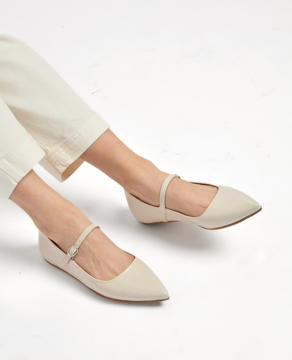 A pair of sleek, pointed-toe flats in a soft beige color, featuring a smooth leather texture, a thin ankle strap with a small buckle, and a low-profile design.