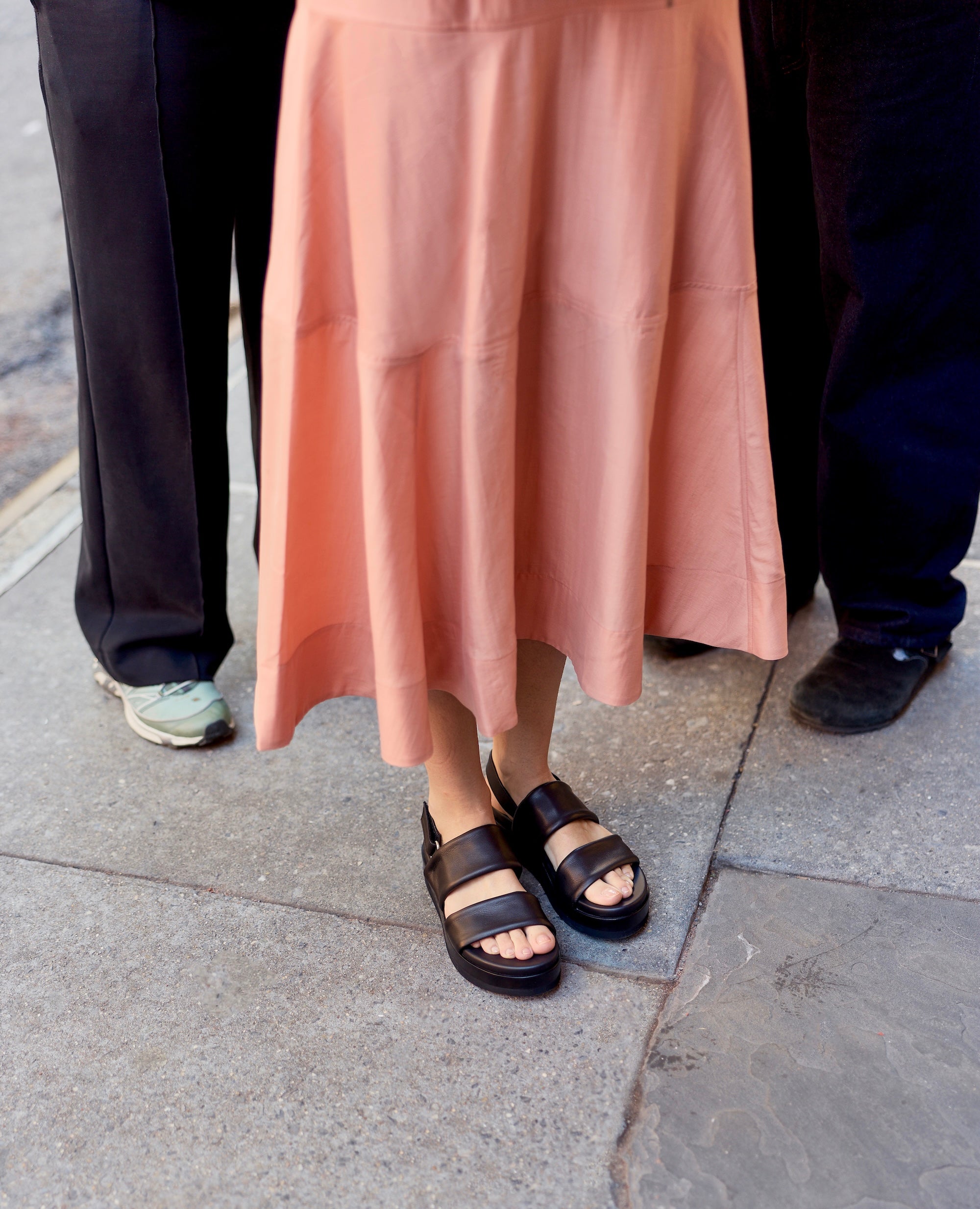 Person wearing black tubular leather sandals on a stone pavement