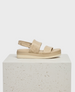 A beige sandal with a thick, cushioned sole, featuring two wide, padded straps across the foot and an adjustable slingback strap, all made from smooth leather. 1