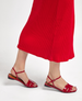 Red sandals with a flat sole, featuring thin straps and a buckle closure, complement a red pleated skirt. 2