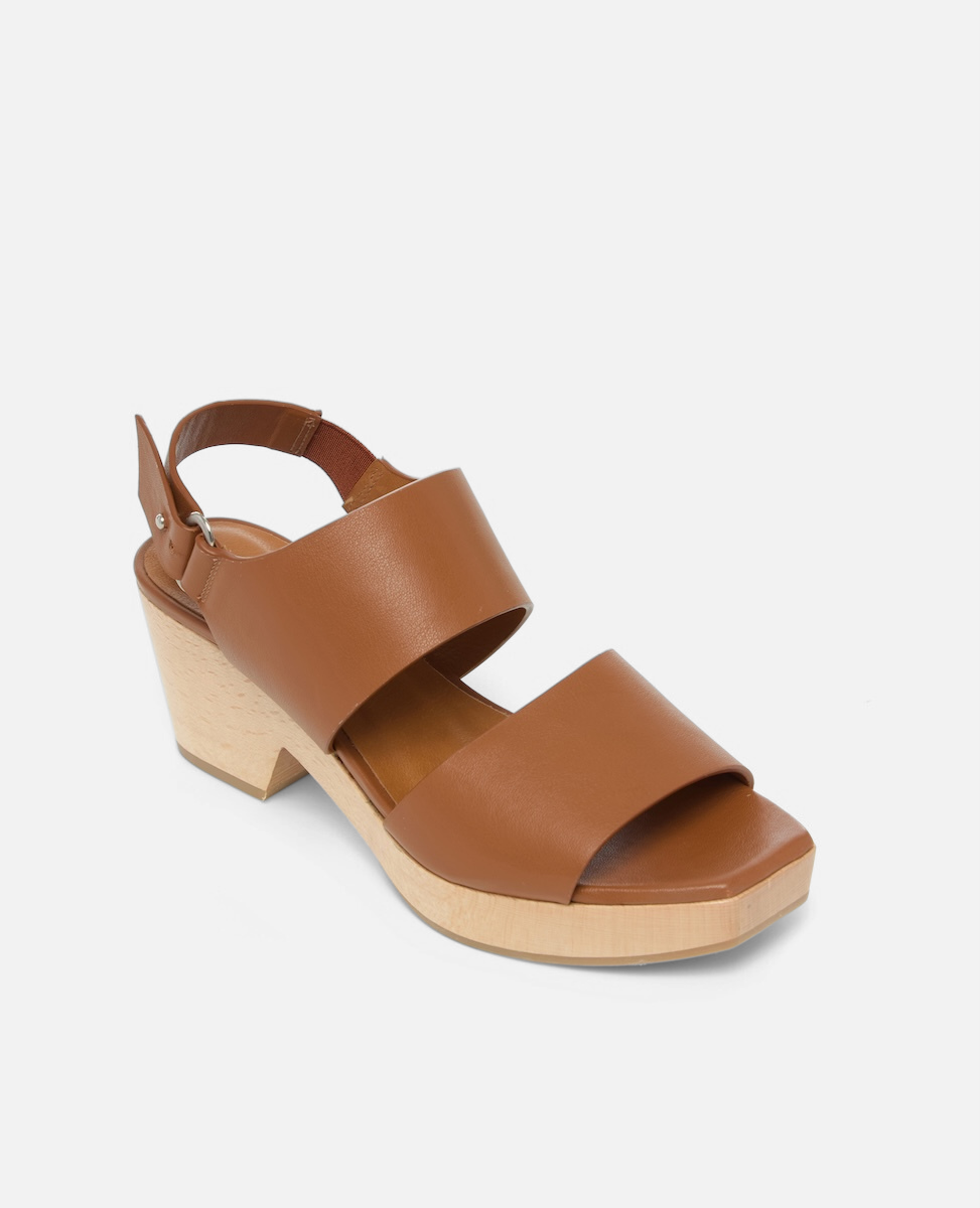A brown leather clog sandal with a chunky wooden heel, featuring a wide front strap, an adjustable ankle strap with a buckle, and a smooth, matte finish.
