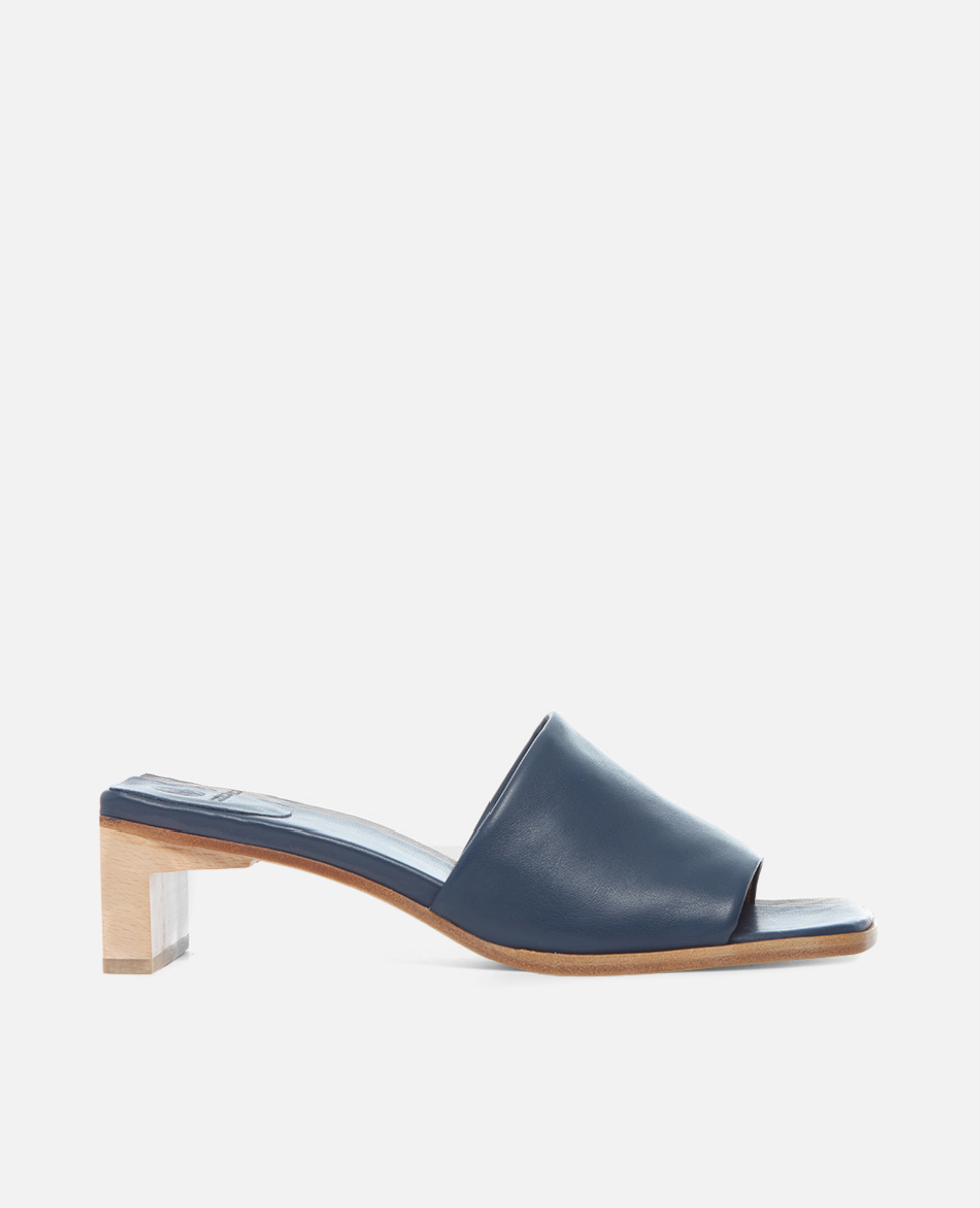 A sleek, navy blue leather mule with an open toe design, featuring a low, block wooden heel and a smooth, minimalist finish.