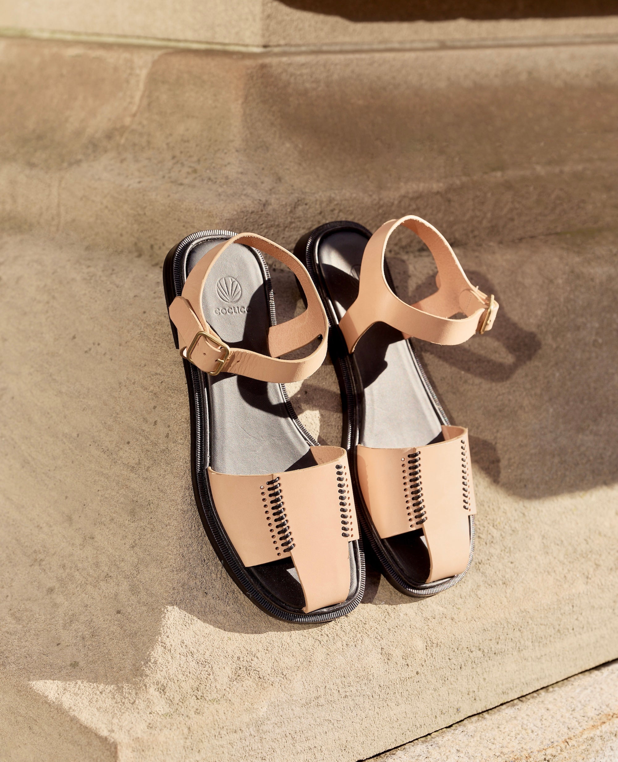 Pair of natural and black leather fisherman sandals on a stone surface